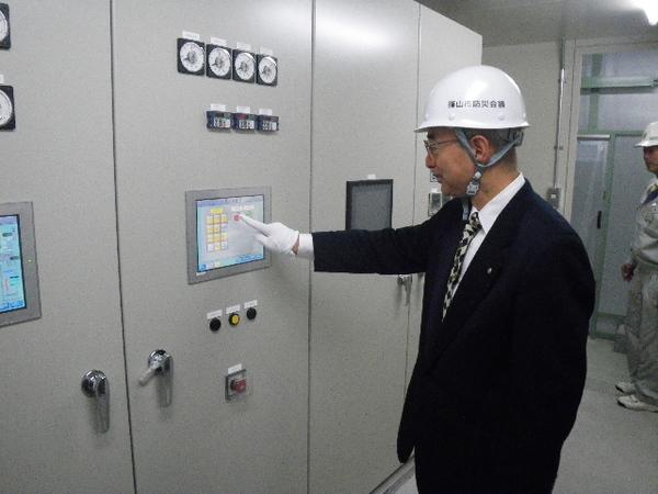 スーツにヘルメットをかぶった市長が機械に指を指している写真